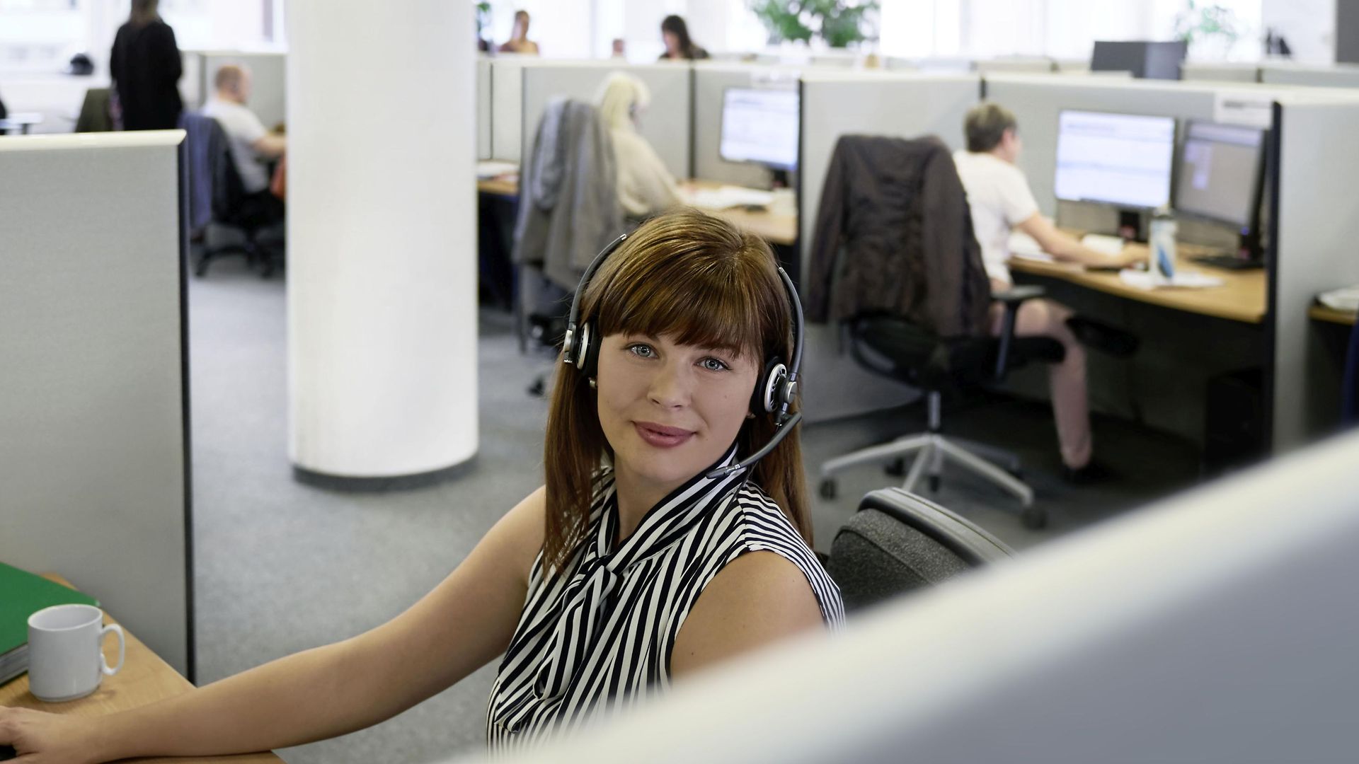 Eine junge DB Call Center Agentin sitzt mit Ihrem headset an Ihrem Computer.