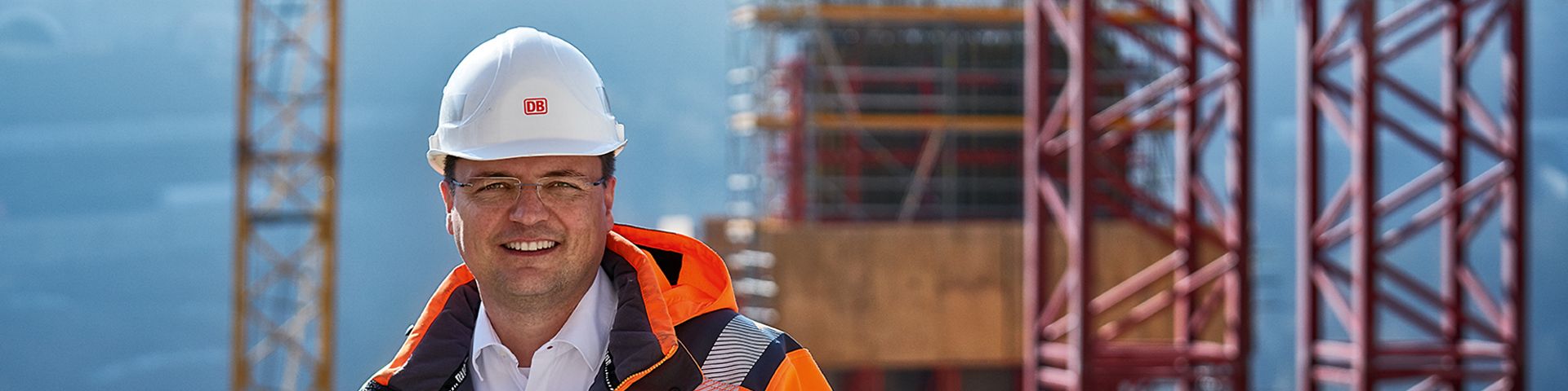 Ein Bauingenieur steht in Warnkleidung und mit Schutzhelm vor einer Baustelle