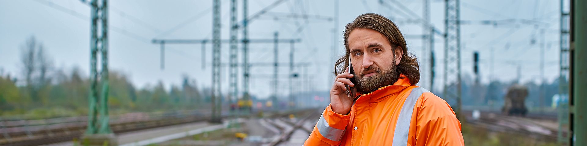 Ein Elektroingenieur steht in Warnkleidung am Gleis und telefoniert