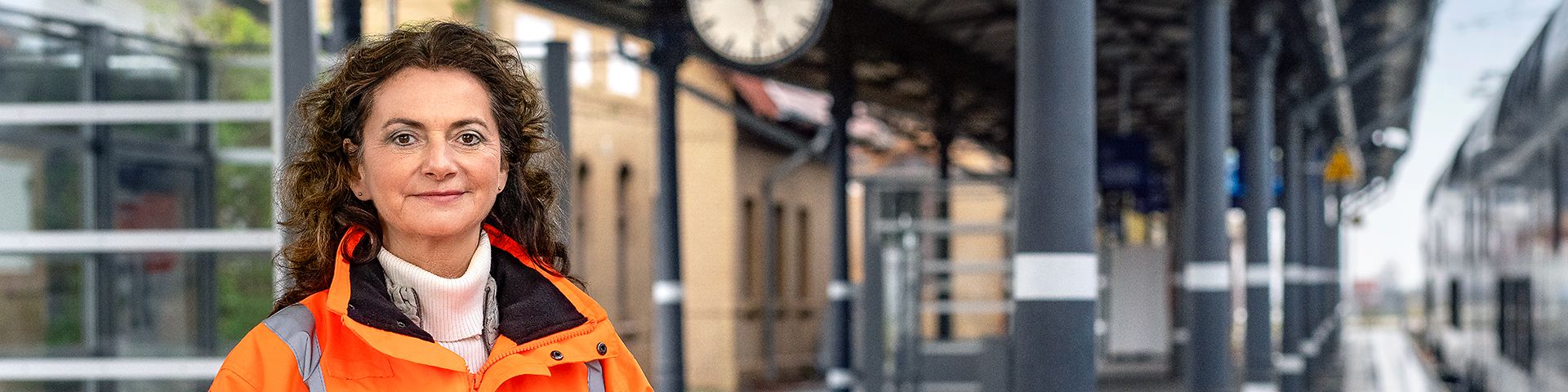Eine Projektingenieurin steht in Warnkleidung am Bahnsteig eines Bahnhofs