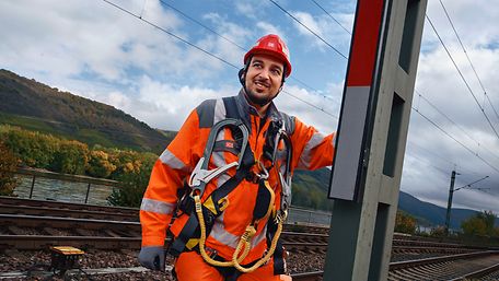 Ein Signalmechaniker in Warnkleidung und mit Schutzhelm steht auf einer Hebebühne