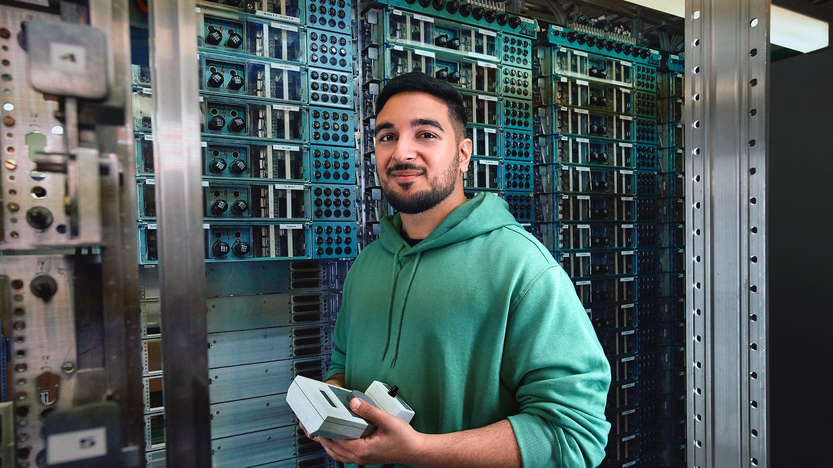 Ein Signalmechaniker steht vor einem Relaisschrank und hält ein elektronisches Diagnosegerät in der Hand