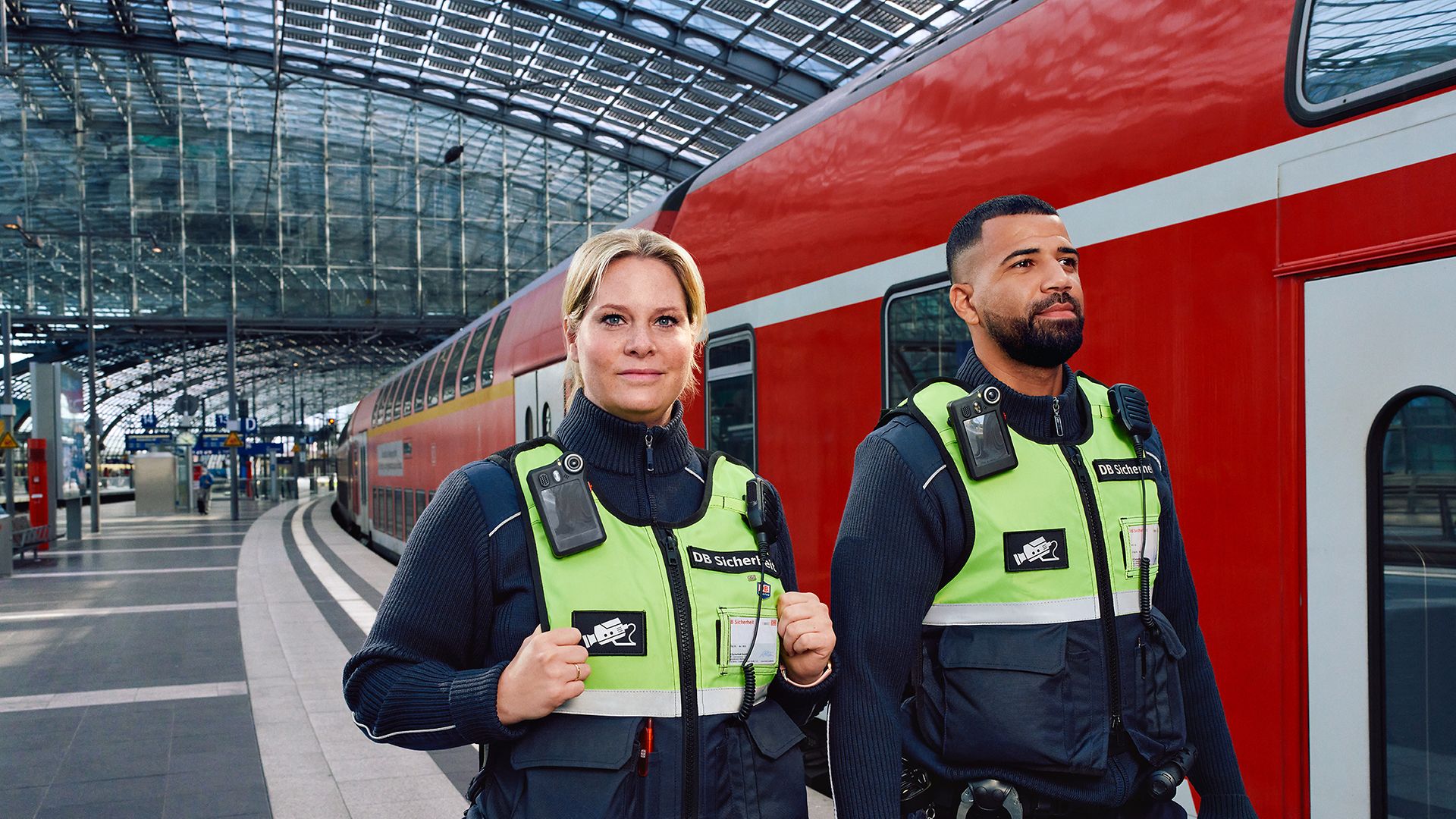 Eine männliche und eine weibliche Fachkraft für Sicherheit stehen vor einer Regionalbahn.