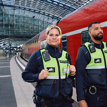 Eine männliche und eine weibliche Fachkraft für Sicherheit stehen vor einer Regionalbahn.