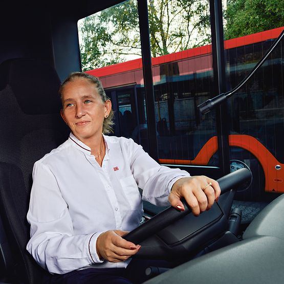 Eine Busfahrerin in Unternehmensbekleidung sitzt am Steuer des Busses