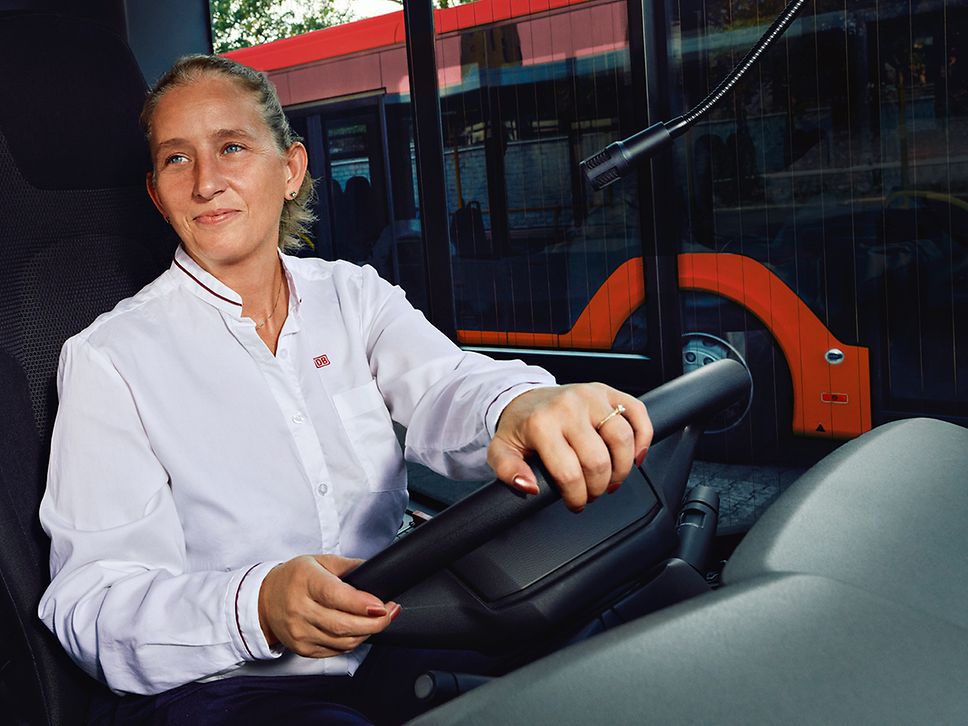 Eine Busfahrerin in Unternehmensbekleidung sitzt am Steuer des Busses