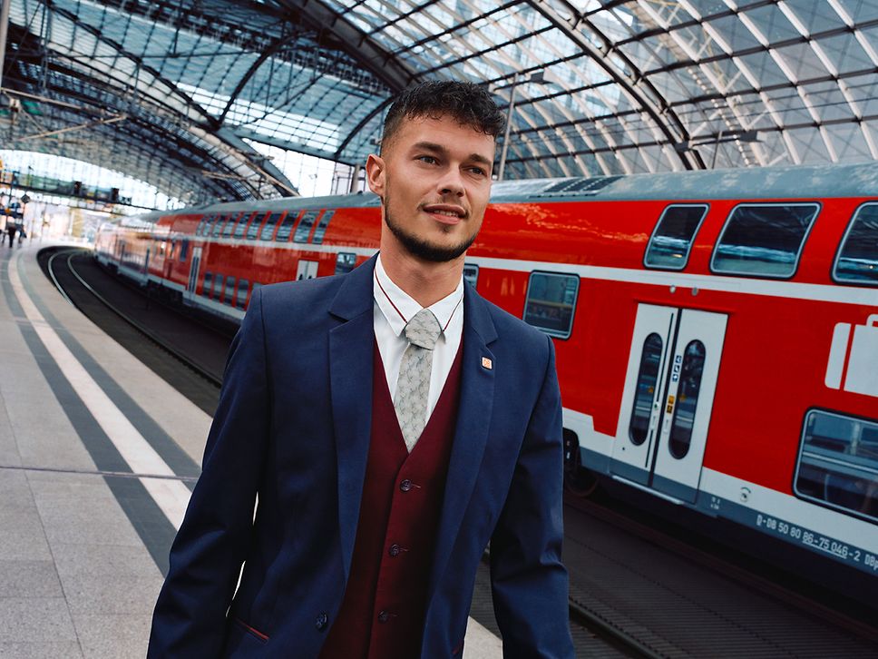 Ein Leiter Bahnhofsservice in Unternehmensbekleidung läuft am Bahnsteig eines Bahnhofs an einem Regionalzug vorbei