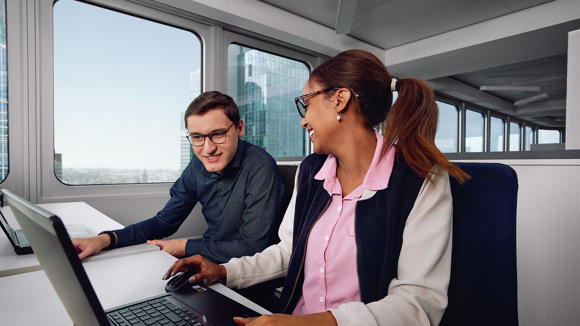 Eine Auszubildende Fachinformatikerin für Anwendungsentwicklung sitzt am Laptop und zeigt ihrem Kollegen etwas