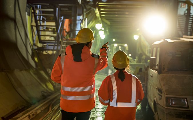 Zwei Ingenieure stehen in Warnkleidung und mit Schutzhelm zeigen auf eine Baustelle