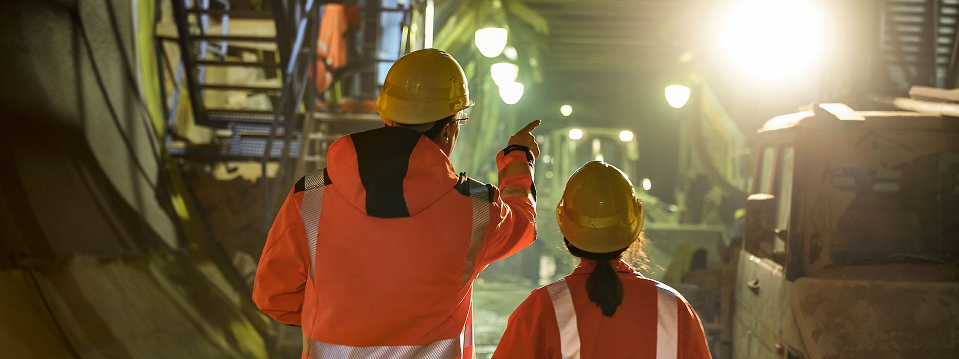 Zwei Ingenieure stehen in Warnkleidung und mit Schutzhelm zeigen auf eine Baustelle