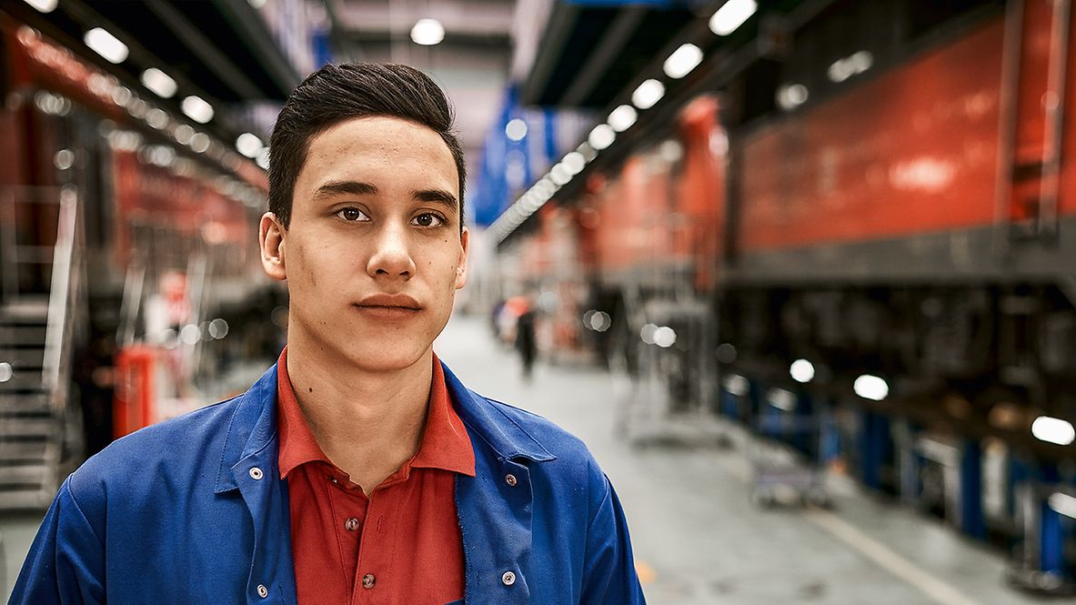Ein Auszubildender zum Mechatroniker steht in Arbeitskleidung in einer Werkshalle