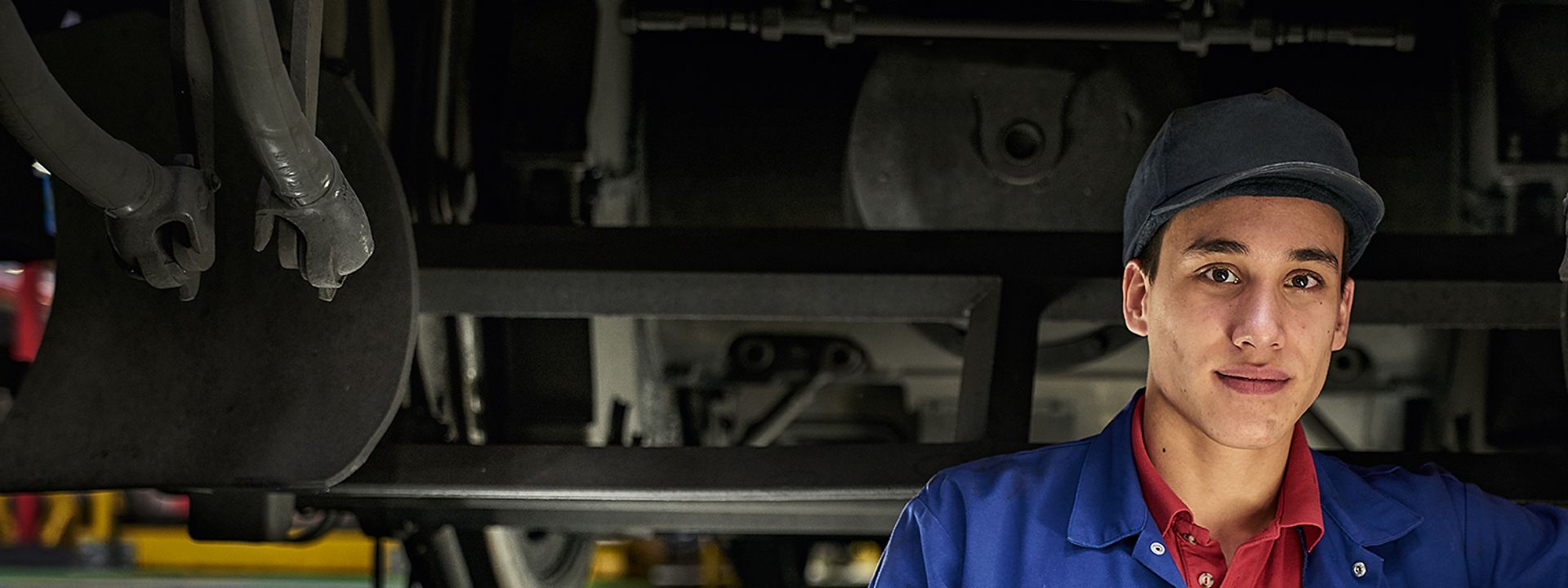 Ein Auszubildender zum Mechatroniker steht in Arbeitskleidung unter einem Zug.