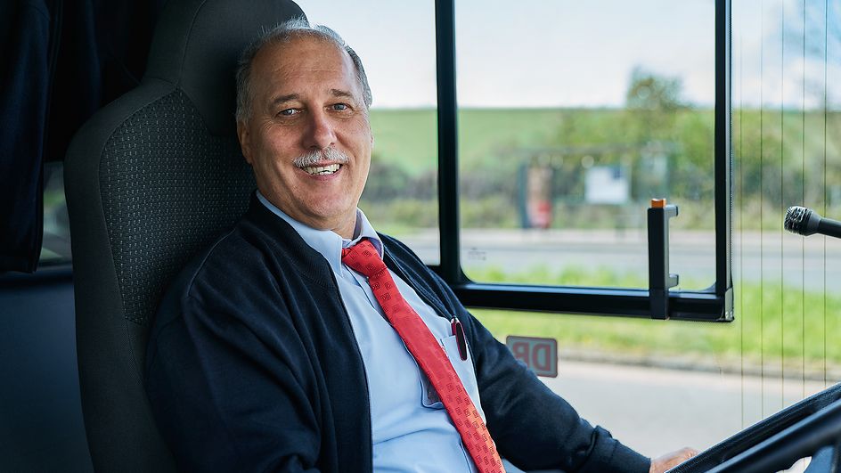Ein Busfahrer sitzt lächelnd auf dem Fahrersitz eines Busses
