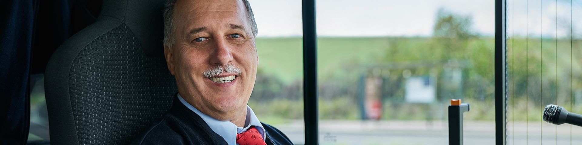 Ein Busfahrer sitzt lächelnd auf dem Fahrersitz eines Busses