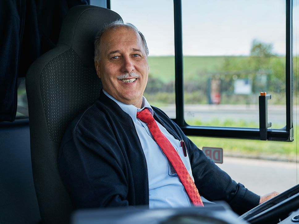 Ein Busfahrer sitzt lächelnd auf dem Fahrersitz eines Busses