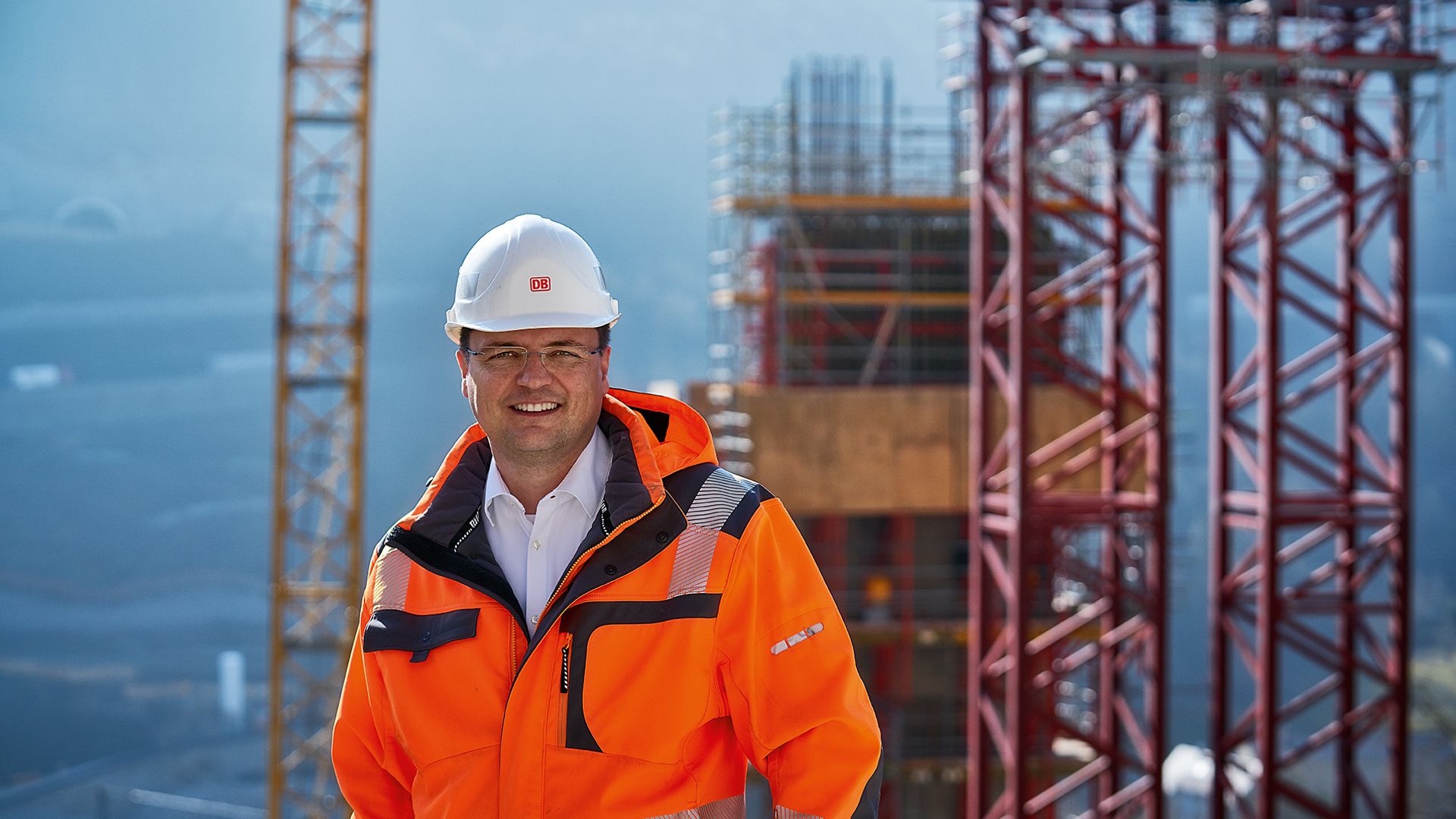 Ein Bauingenieur steht in Warnkleidung und mit Schutzhelm vor einer Baustelle
