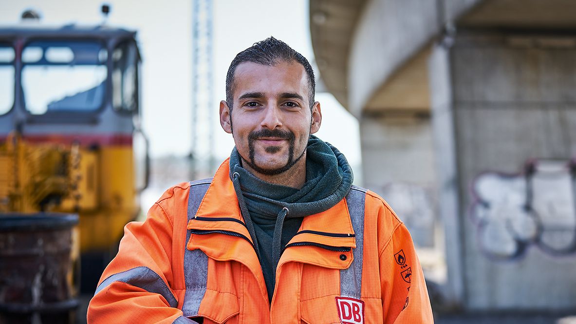 Ein Gleisbauer steht in Warnweste vor einem Instandhaltungsfahrzeug