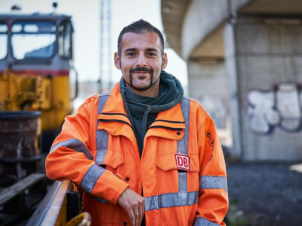 Ein Gleisbauer steht in Warnweste vor einem Instandhaltungsfahrzeug