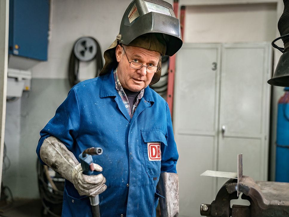 Ein Industriemechaniker steht in der Werkstatt, trägt eine Schweißermaske und hält ein Schweißgerät in der Hand