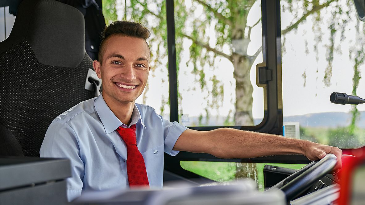 Ein Auszubildender zum Busfahrer sitzt in Unternehmensbekleidung am Steuer eines Busses