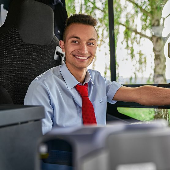 Ein Auszubildender zum Busfahrer sitzt in Unternehmensbekleidung am Steuer eines Busses