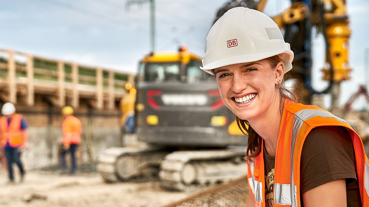 Eine Dualstudierende Bauingenieurwesen steht in Warnkleidung und mit Schutzhelm auf einer Baustelle
