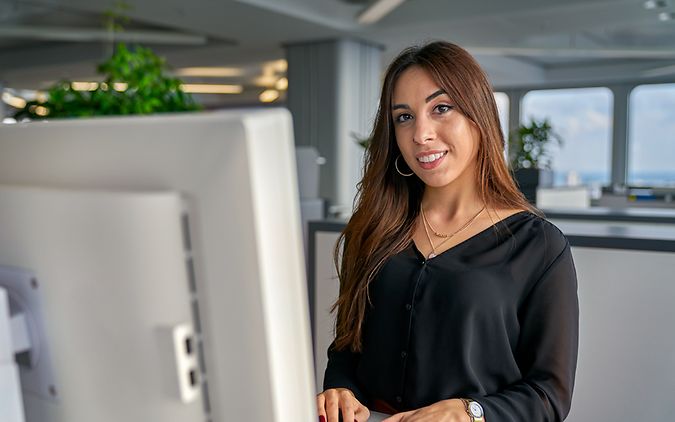 Eine Auszubildende zur Industriekauffrau steht vor einem Bildschirm in einem Büro