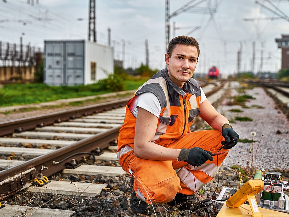 Ein Elektroniker für Leit- und Sicherungstechnik in Warnkleidung kniet neben dem Gleis