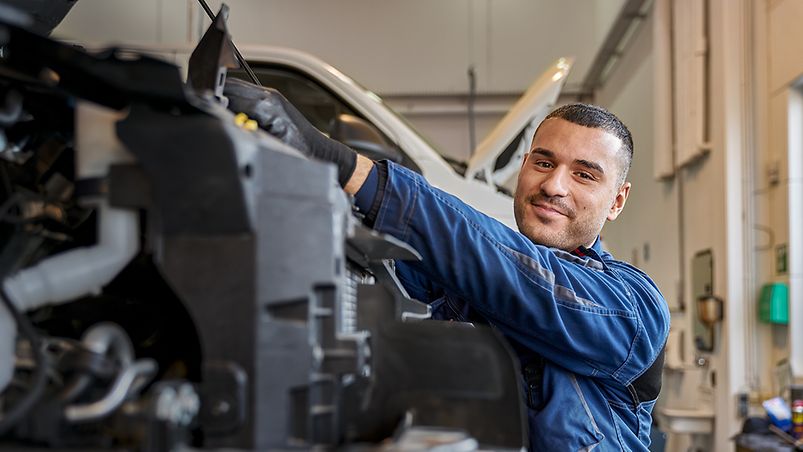 Ein KFZ-Mechatroniker in Arbeitsbekleidung arbeitet in einer Werkstatt an einem Motor