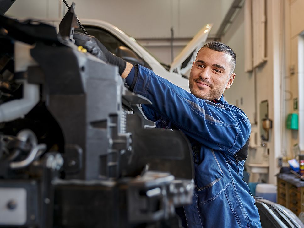 Ein KFZ-Mechatroniker in Arbeitsbekleidung arbeitet in einer Werkstatt an einem Motor
