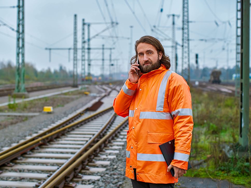 Ein Elektroingenieur steht in Warnkleidung am Gleis und telefoniert