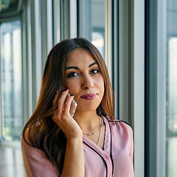 Eine Auszubildende zur Immobilienkauffrau steht vor dem Fenster eines Büros und telefoniert.
