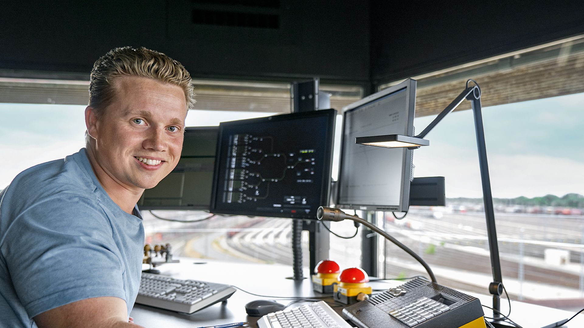 Ein Auszubildender zum Fahrdienstleiter steht vor drei Bildschirmen in einem Stellwerk