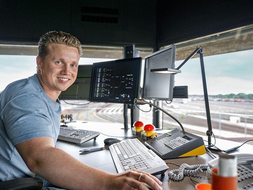 Ein Auszubildender zum Fahrdienstleiter steht vor drei Bildschirmen in einem Stellwerk