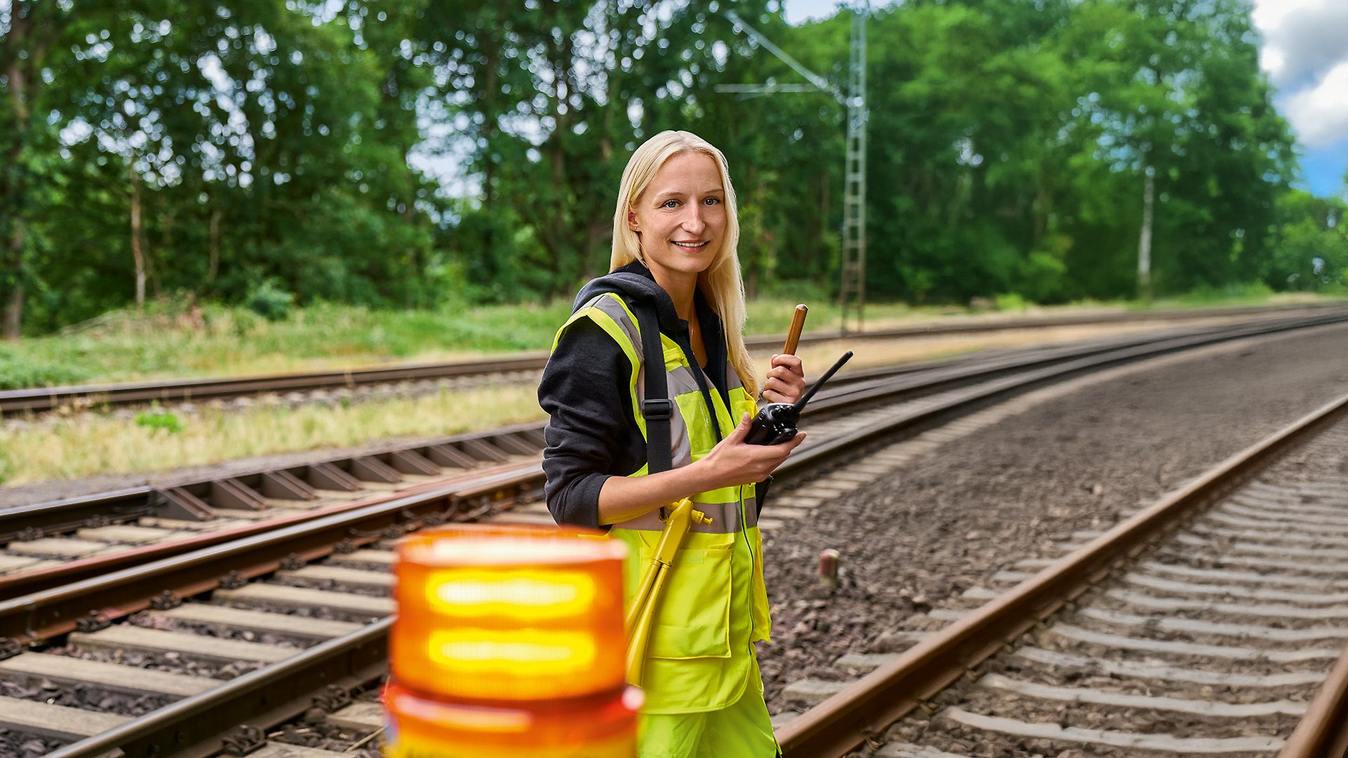Eine Frau in Warnweste steht als Sicherungsposten am Waldrand neben dem Gleis