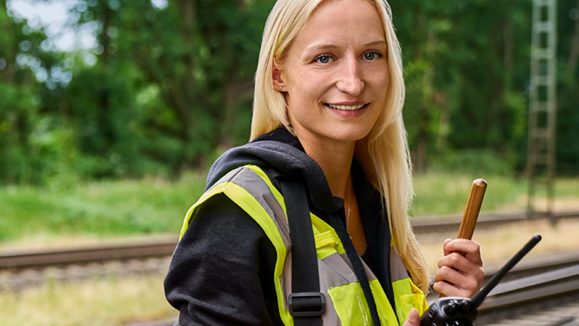 Eine Frau in Warnweste steht als Sicherungsposten am Waldrand neben dem Gleis