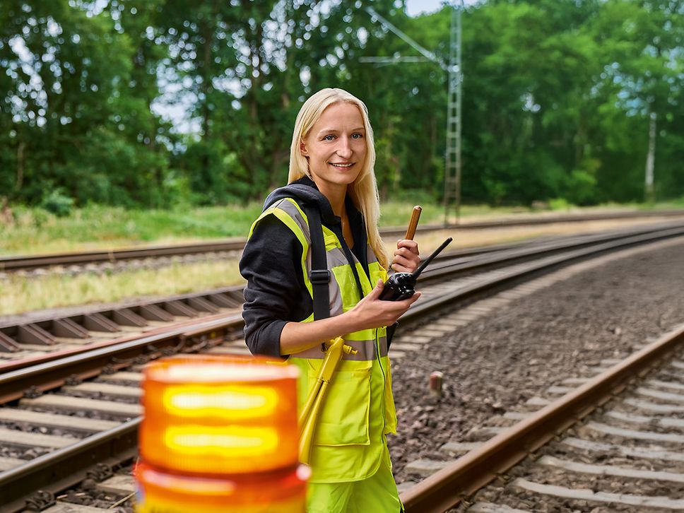 Eine Frau in Warnweste steht als Sicherungsposten am Waldrand neben dem Gleis