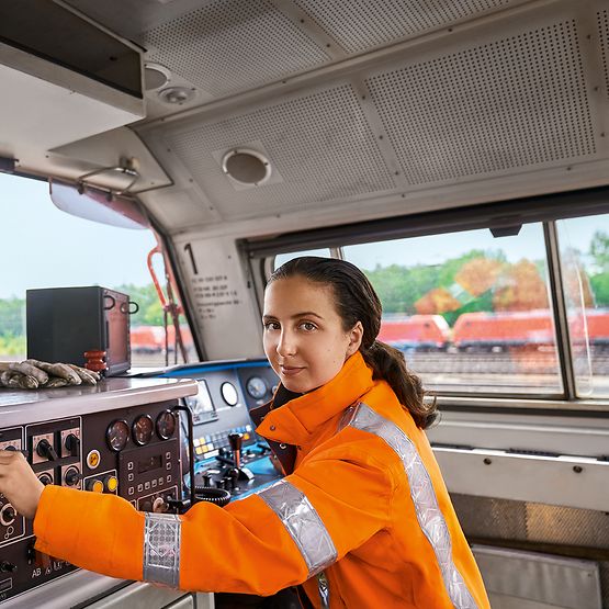 Eine Auszubildende zur Lokführerin im Güterverkehr stellt im Führerstand eines Güterverkehrszuges die Bordelektronik ein