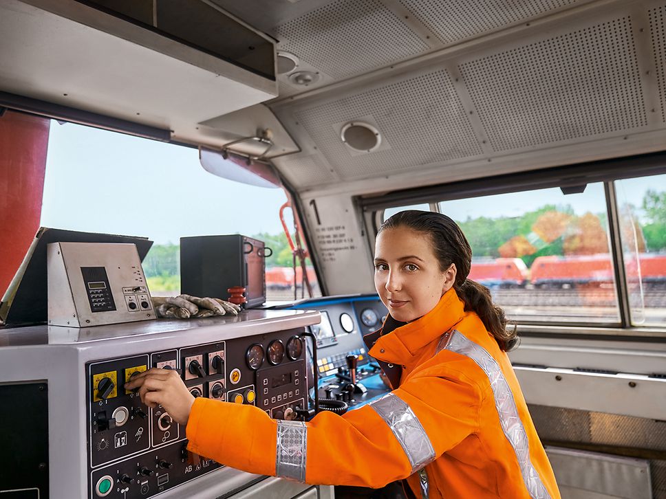 Eine Auszubildende zur Lokführerin im Güterverkehr stellt im Führerstand eines Güterverkehrszuges die Bordelektronik ein