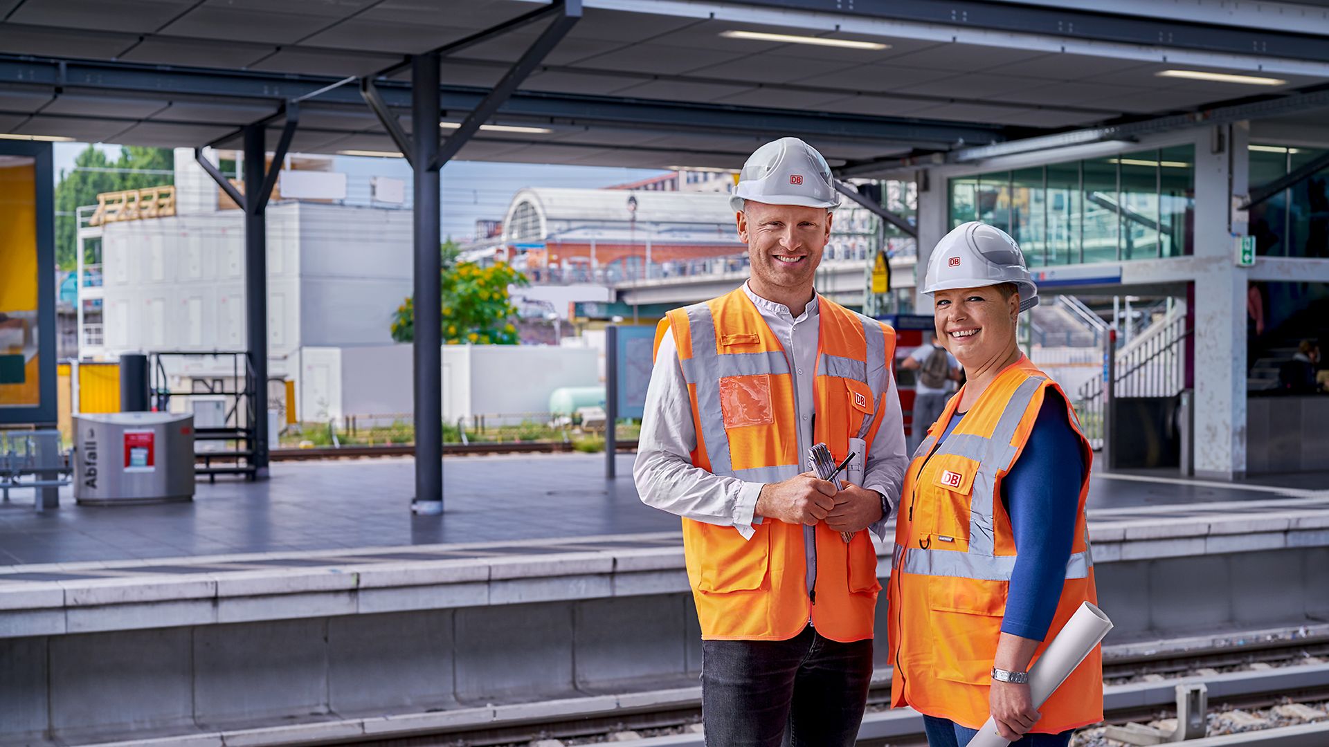 Zwei Bauingenieure stehen in Warnkleidung und mit Schutzhelm am Bahnsteig eines Bahnhofs