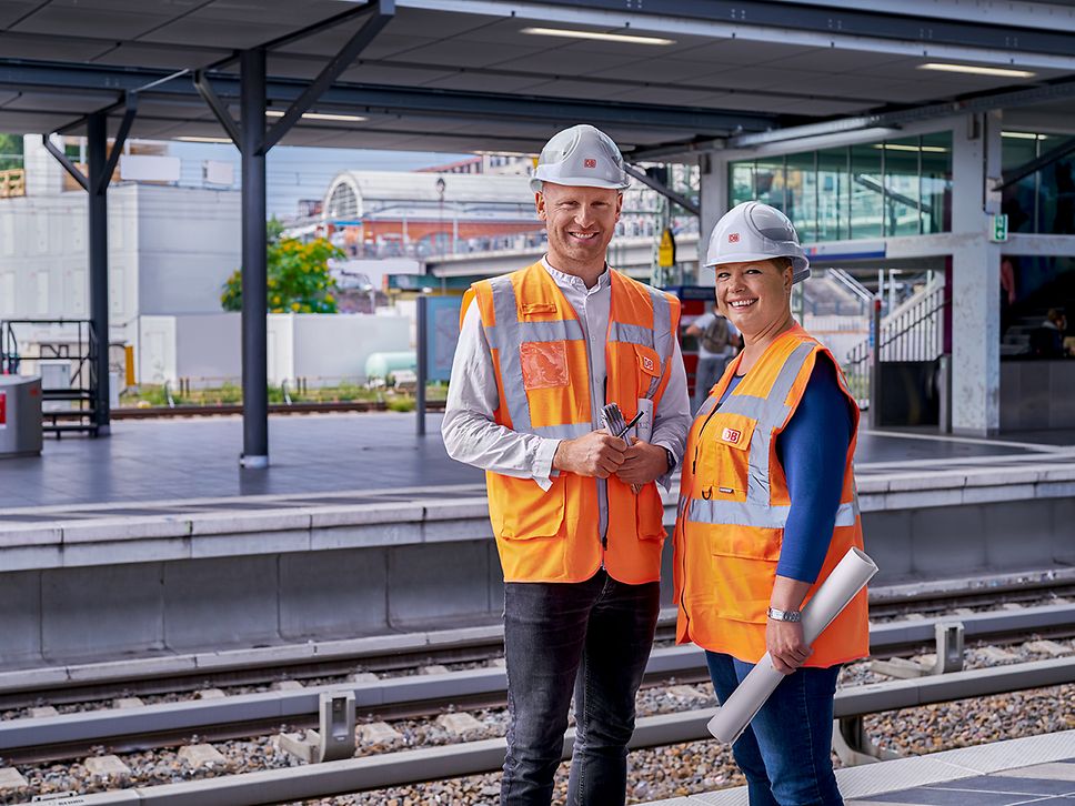 Zwei Bauingenieure stehen in Warnkleidung und mit Schutzhelm am Bahnsteig eines Bahnhofs