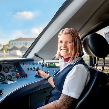 Eine Lokführerin im Regionalverkehr in Unternehmensbekleidung sitzt im Führerstand eines Triebfahrzeuges