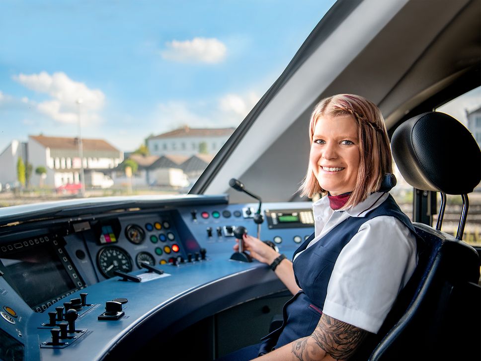 Eine Lokführerin im Regionalverkehr in Unternehmensbekleidung sitzt im Führerstand eines Triebfahrzeuges