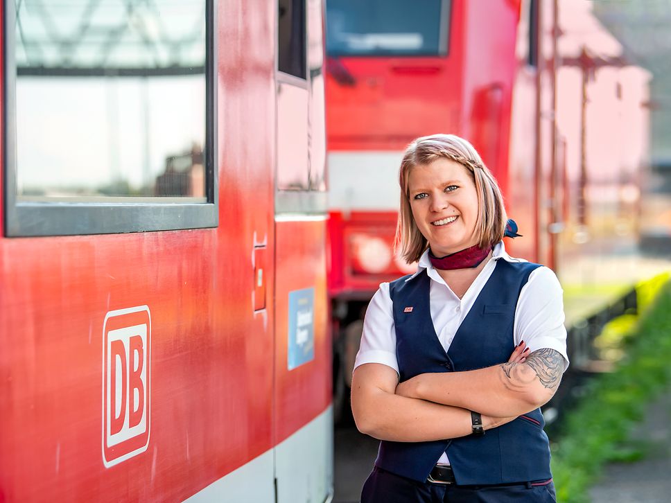 Eine Lokführerin in Unternehmensbekleidung steht neben einem Zug des Regionalverkehrs