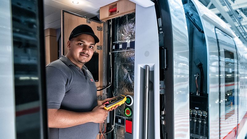 Ein Elektroniker liest die Bordelektronik einer Bildschirmanzeige im Gang eines Zuges aus