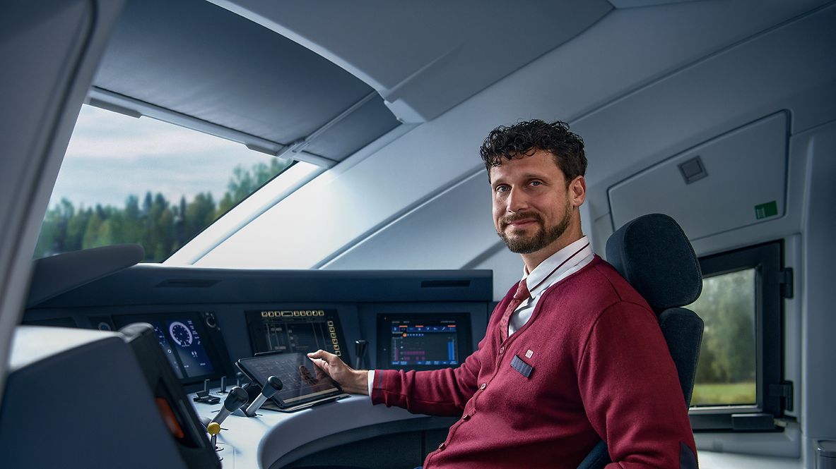 Ein Lokführer in Unternehmensbekleidung sitzt im Führerstand eines ICE