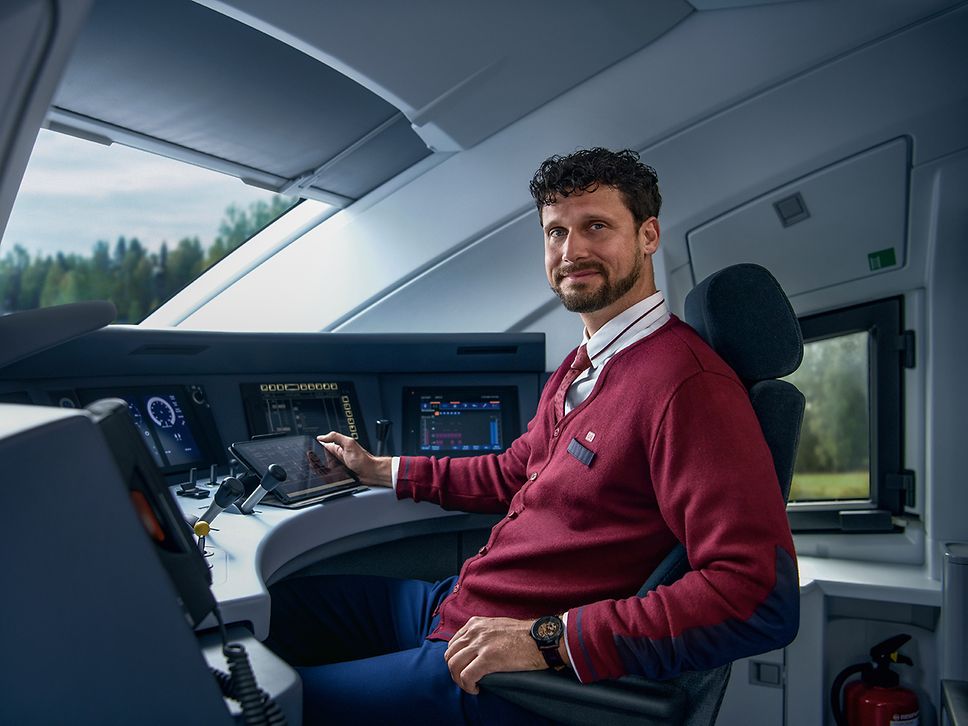 Ein Lokführer in Unternehmensbekleidung sitzt im Führerstand eines ICE