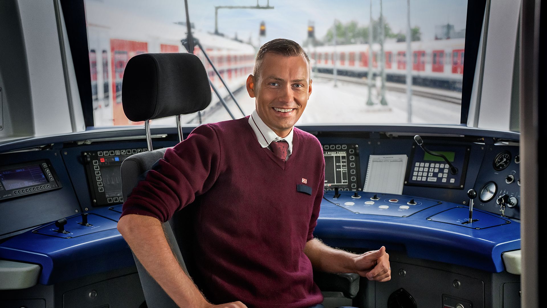 Ein Lokführer sitzt in der Führerkabine eines Regio Zuges und lächelt.