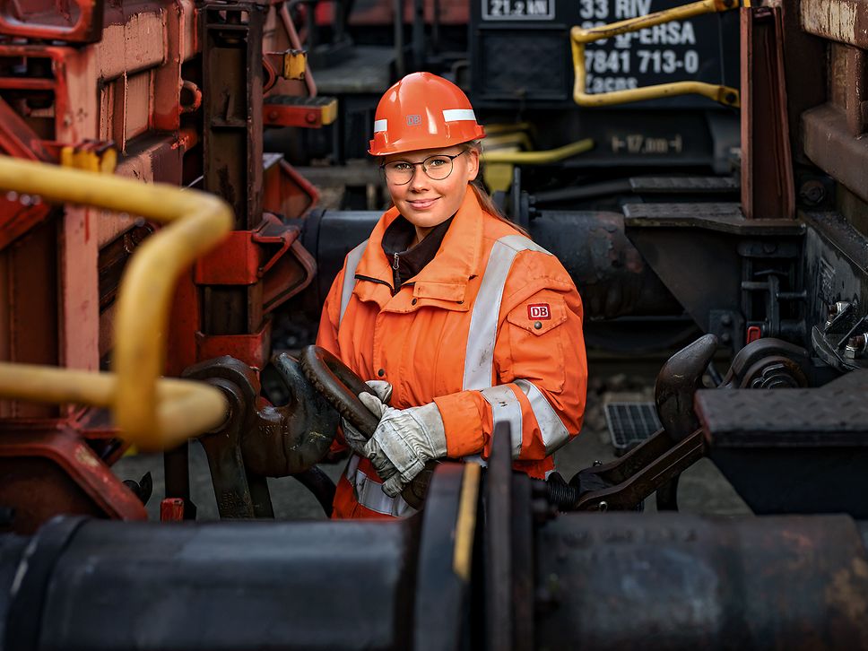Eine Lokrangierführerin in Warnkleidung und mit Schutzhelm steht zwischen zwei Güterloks und kuppelt die Loks aneinander