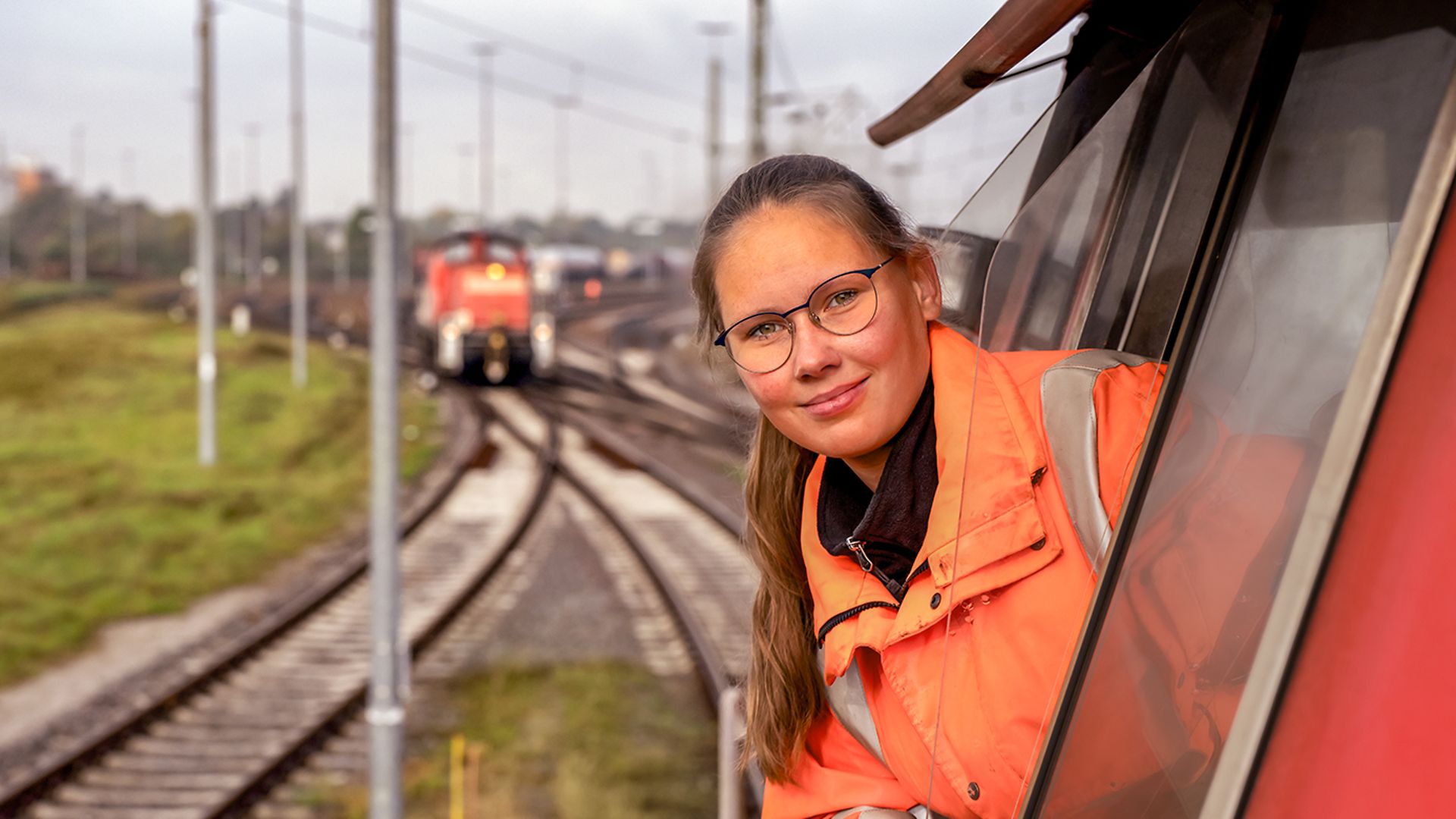 Eine Lokrangierführerin in Warnkleidung sitzt im Führerstand eines Güterzugs und schaut aus dem Fenster